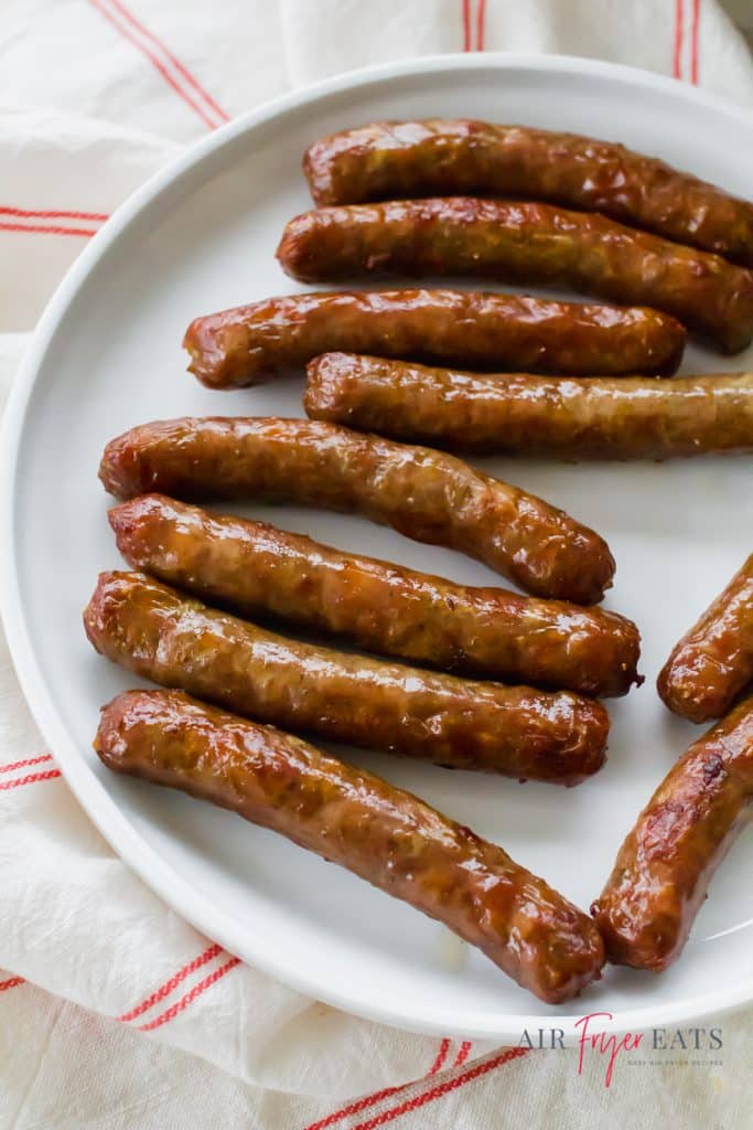 a round white plate topped with 10 cooked sausage links