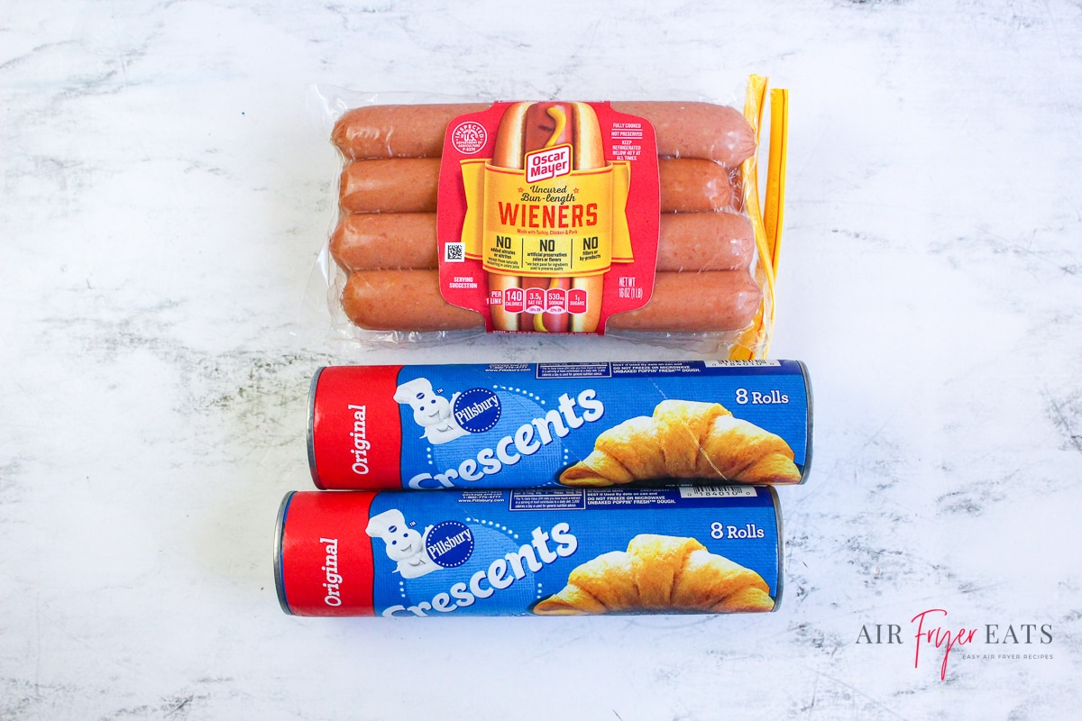 a package of hot dogs and two cans of crescent rolls on a marble countertop