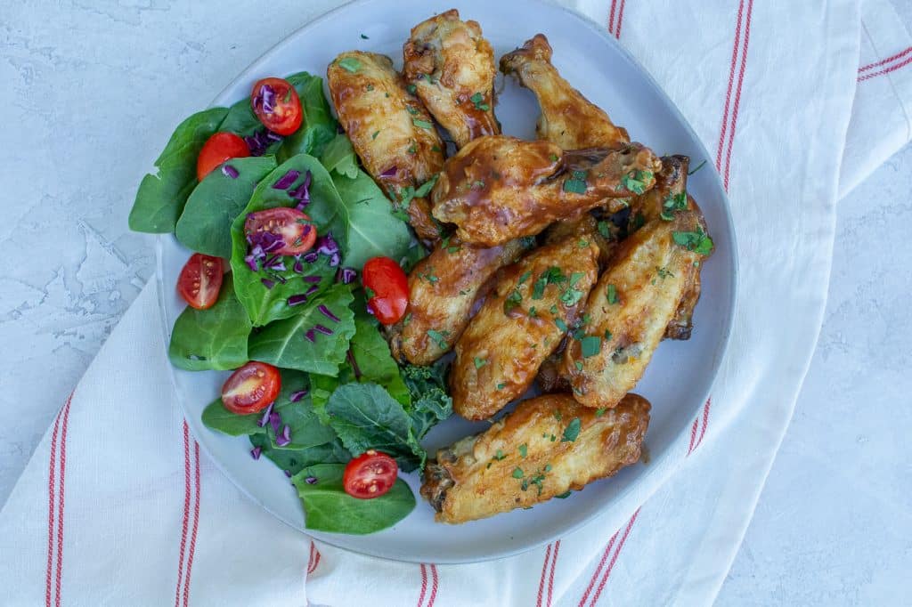 brown glaze covered chicken wings cookedin the air fryer next to a green spinach salad with cut up tomatoes