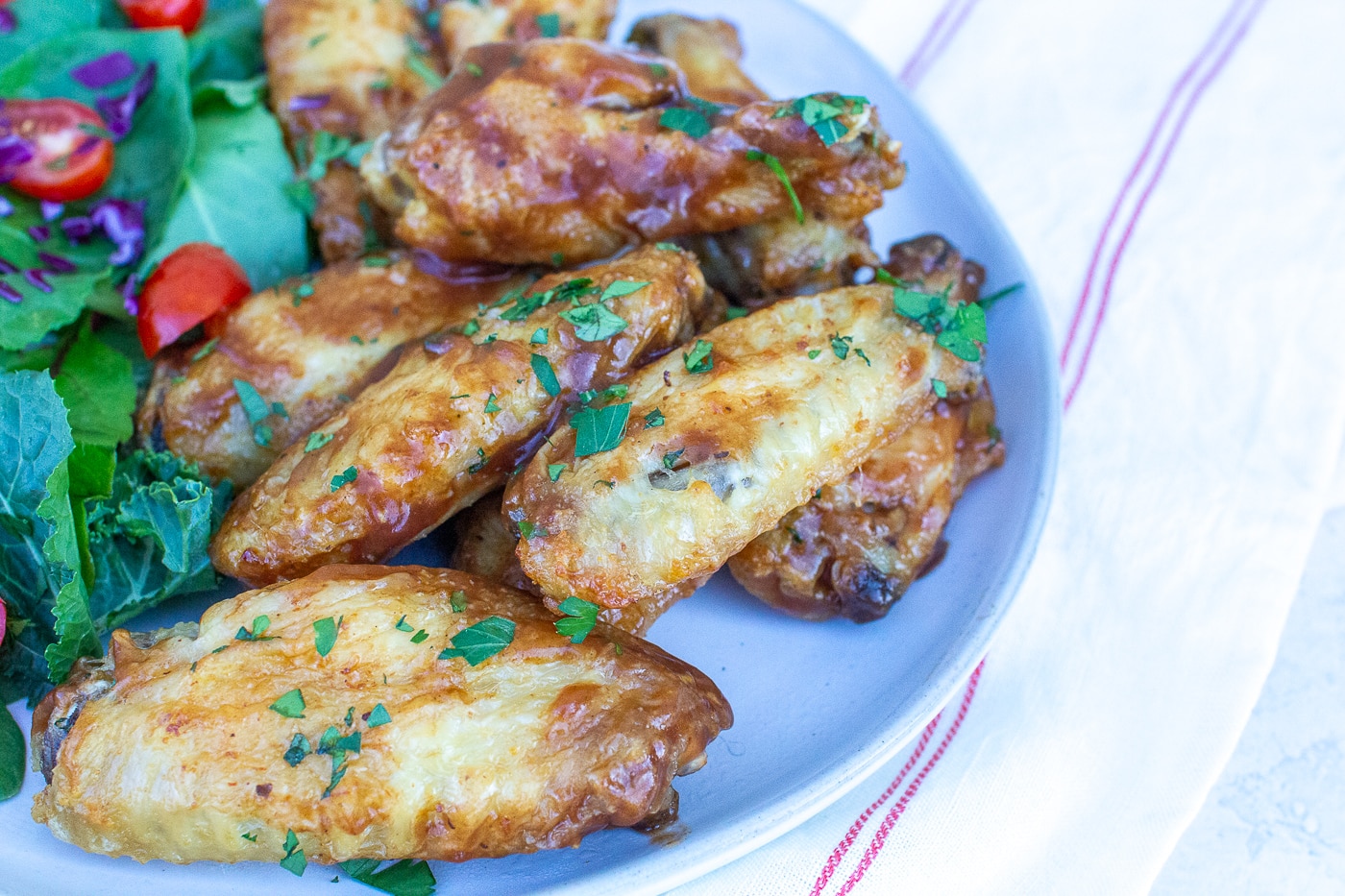 brown glazed chicken wing pieces sprinkled with chopped green herbs aside a green salad
