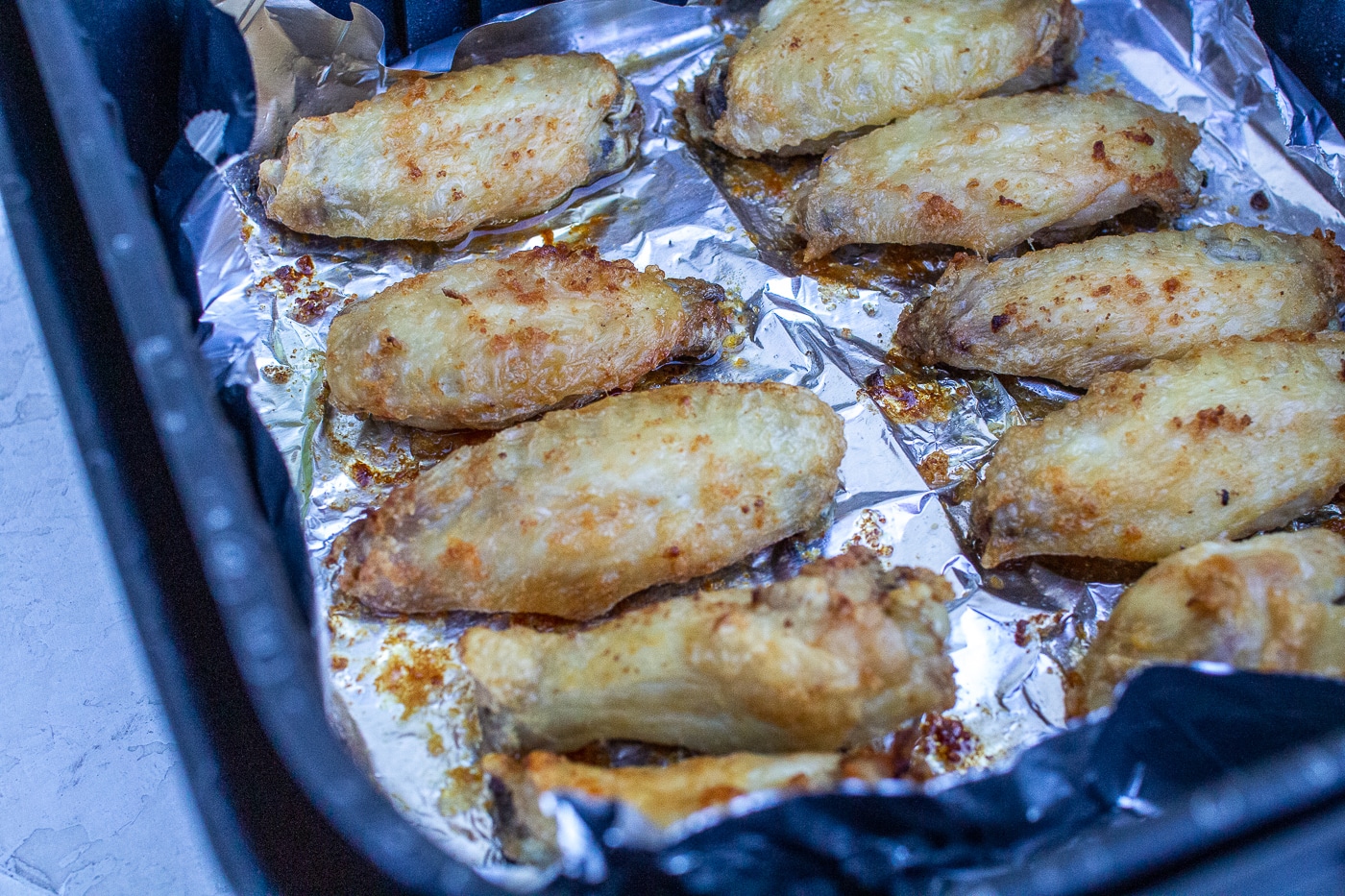 cooked chicken wing pieces arranged in a foil lined air fryer basket