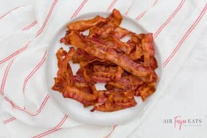 a large pile of crispy brown bacon pieces on a white plate over a striped red and white towel