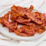 a pile of bacon pieces on a white plate on top of a red and white flour sack cloth
