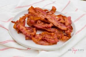 a pile of bacon pieces on a white plate on top of a red and white flour sack cloth