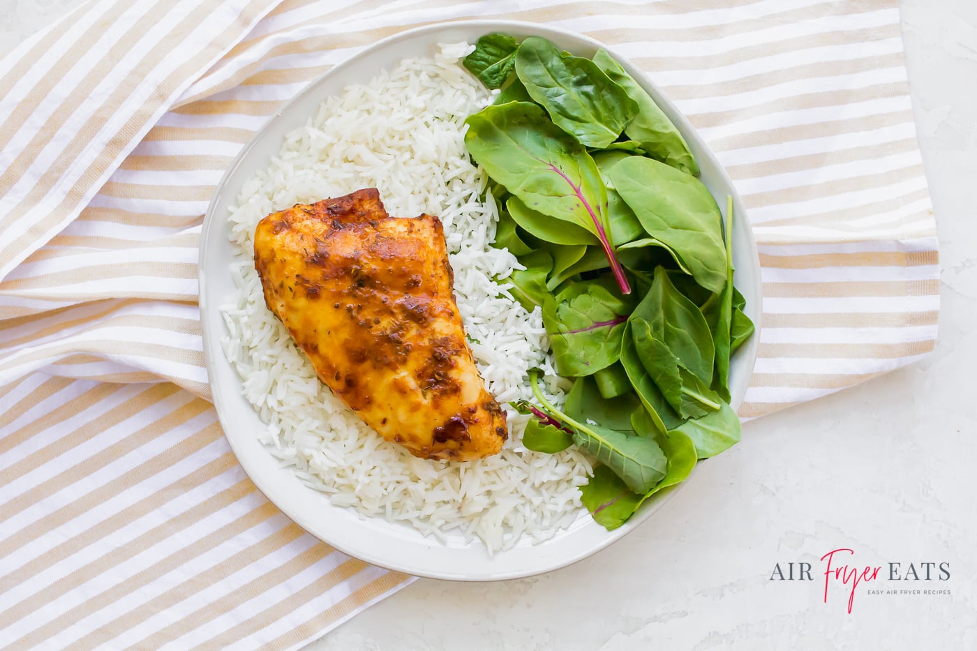 A single chicken breast on a white plate with steamed white rice and a generous helping of fresh spinach