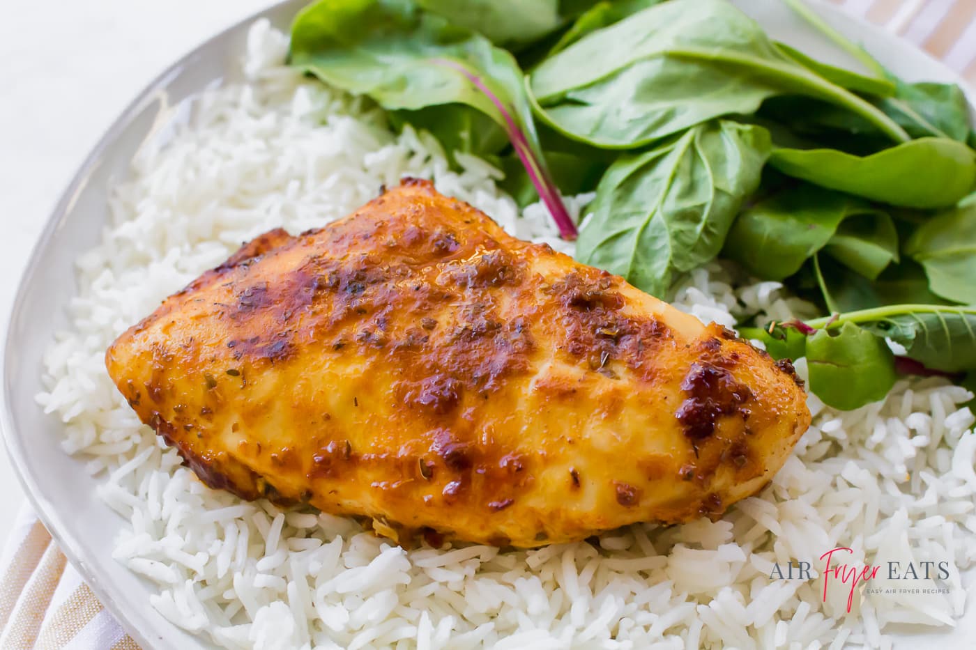 A browned skinless chicken breast on a bed of white rice with fresh greens