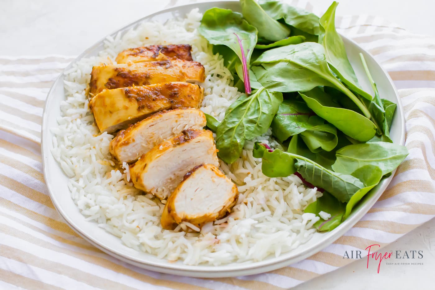 a white plate with a bed of fluffy white rice topped with a sliced chicken breast aside bright green spinach leaves