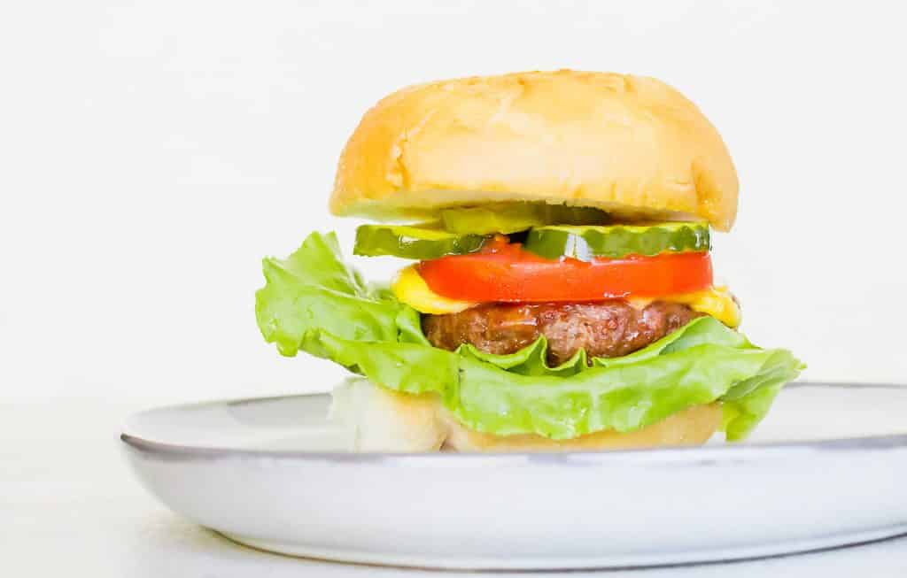 a cheeseburger on a light tan bun with green lettuce, a red tomato slice, and a few slices of green pickle