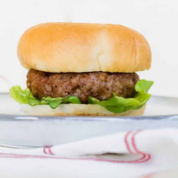 A thick cooked hamburger on a fluffy looking hamburger bun with a piece of green leafy lettuce