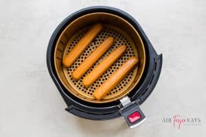 four hot dogs in a round basket of an air fryer