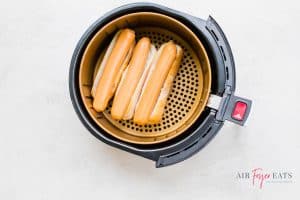 three hot dogs on hot dog buns in an air fryer basket