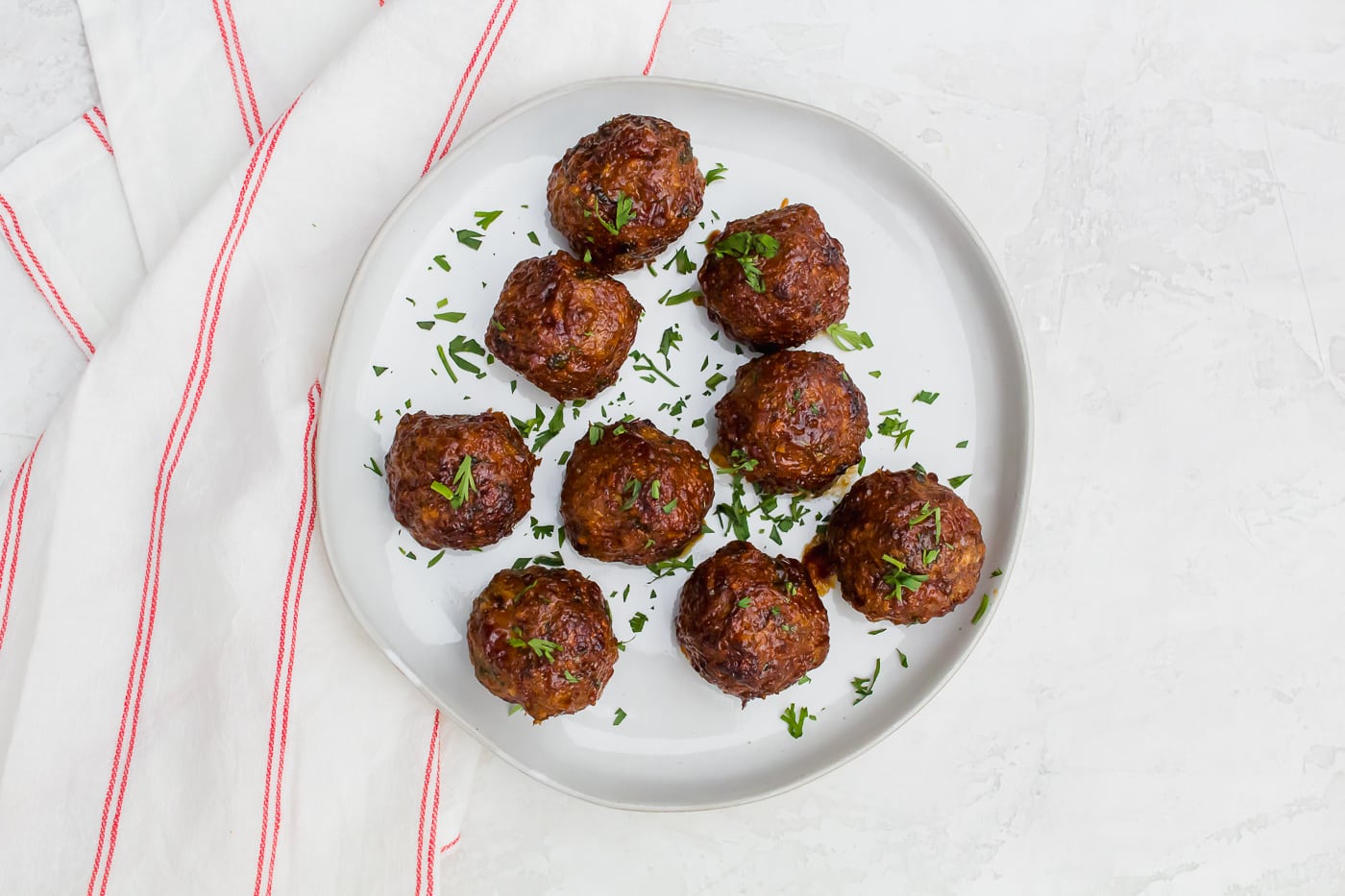 meatballs on a white plate sprinkled with chopped green pieces of parsley