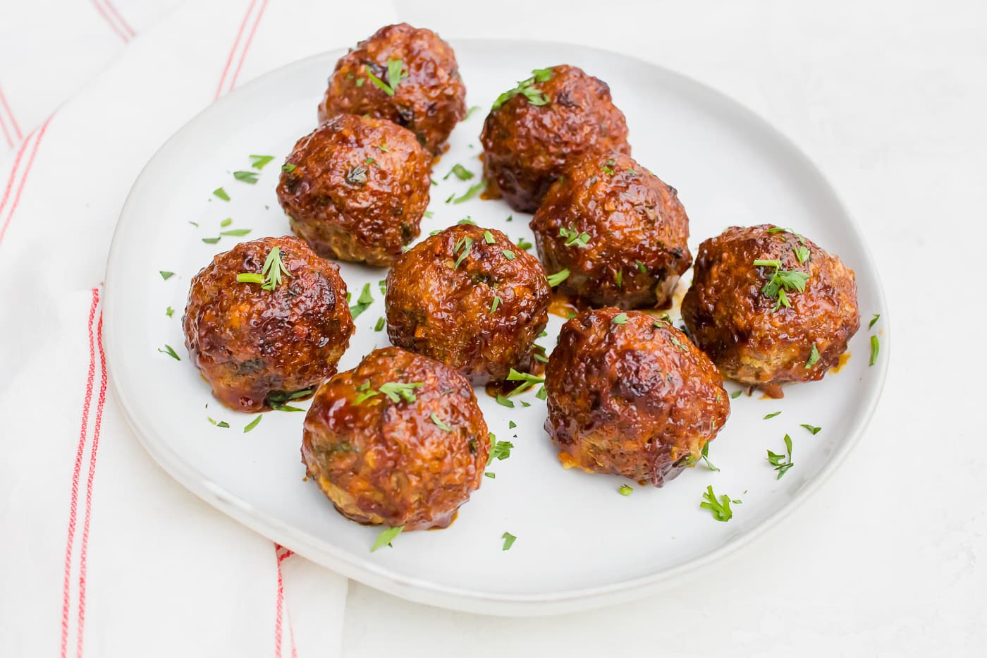 meatballs glazed with a brown-orange sauce and sprinkled with bright green herbs on a white plate