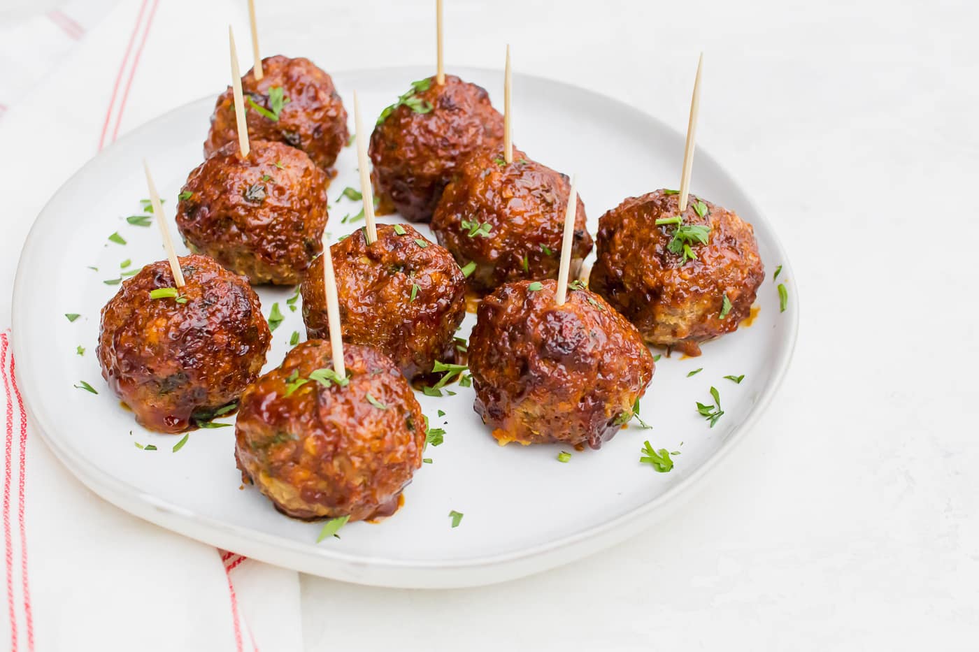 skewered meatballs with a brown glaze and fresh parsley on a bright white round plate