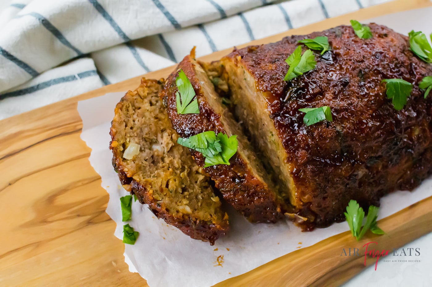 a glazed brown meatloaf topped with chopped herbs on a parchment lined cutting board