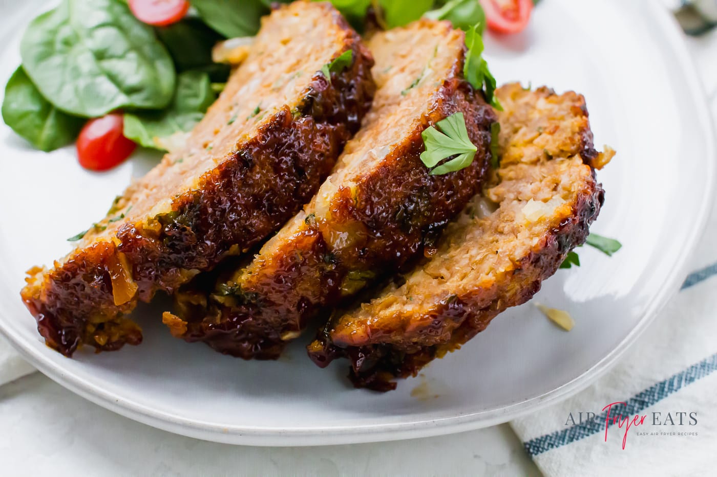 three slices of meatloaf topped with chopped herbs and arranged on a round white plate