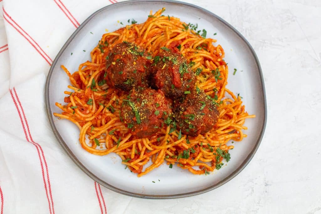 four meatballs sprinkled with green chopped herbs over a pile of spaghetti with red sauce on a white plate