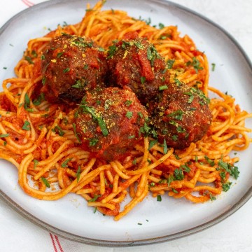 a pile of spaghetti and four meatballs covered in red sauce with fresh herbs on a round white plate