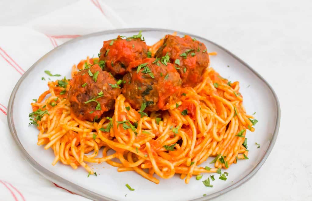 a white plate with a pile of spaghetti topped with meatballs with red sauce