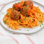 a pile of spaghetti and meatballs in red sauce on a white round plate