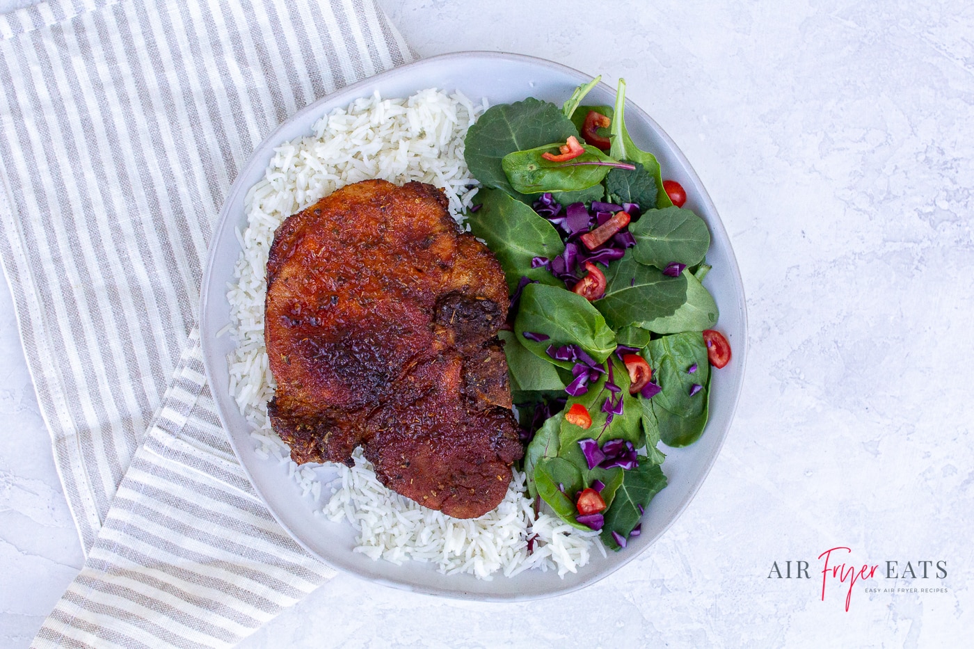 a browned porkchop over a bed of rice with a side salad on a white plate