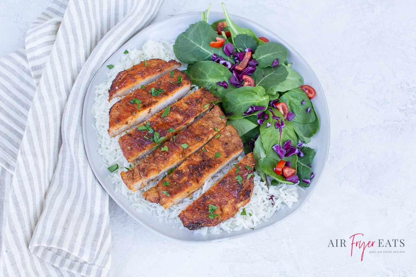 a sliced porkchop on white rice with a spinach salad on the side