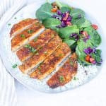 a sliced browned pork chop cutlet with a green spinach salad with chopped vegetables