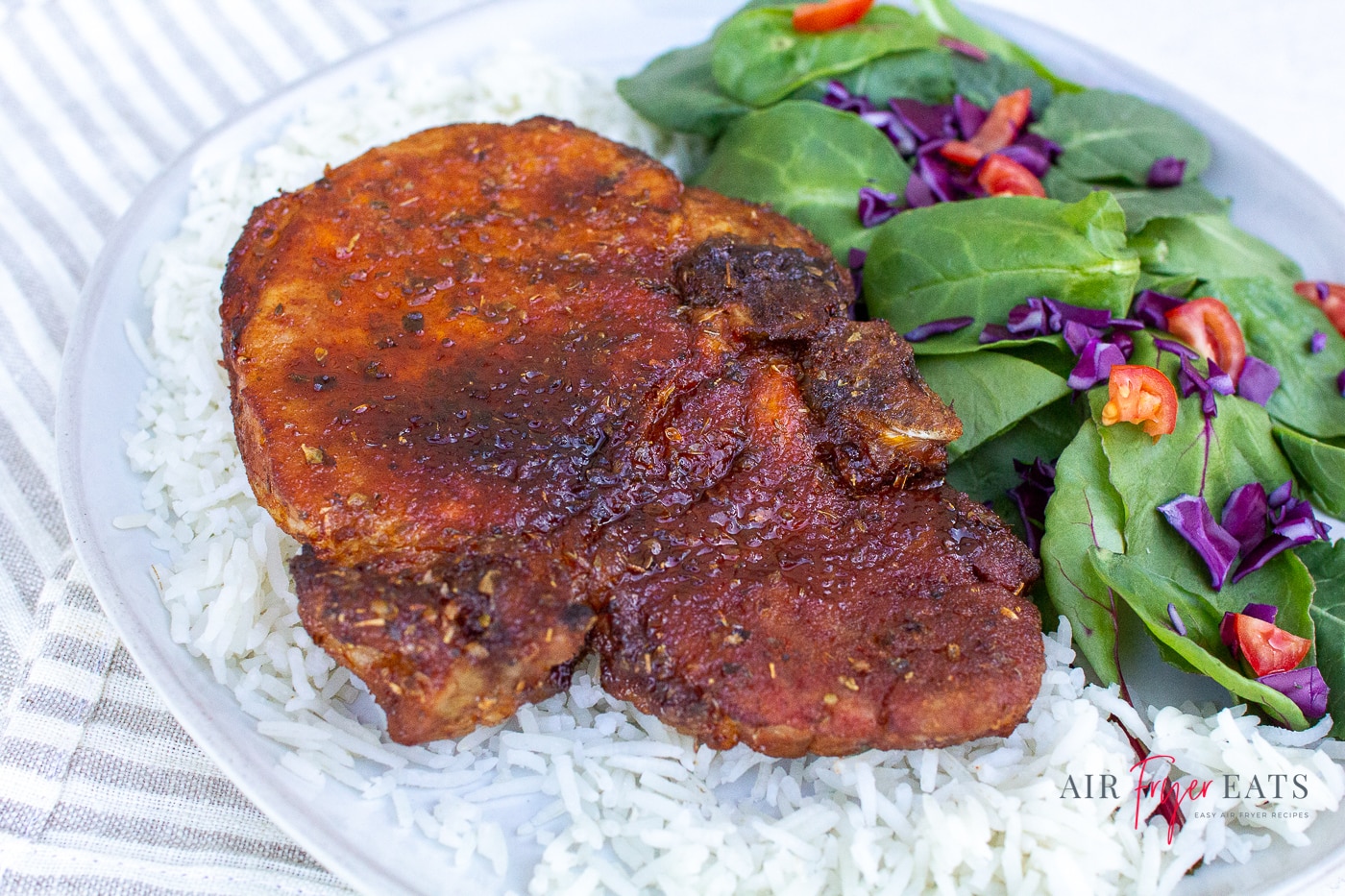 a pork chop with a crispy brown crust aside a spinach and vegetable salad served with fluffy white rice