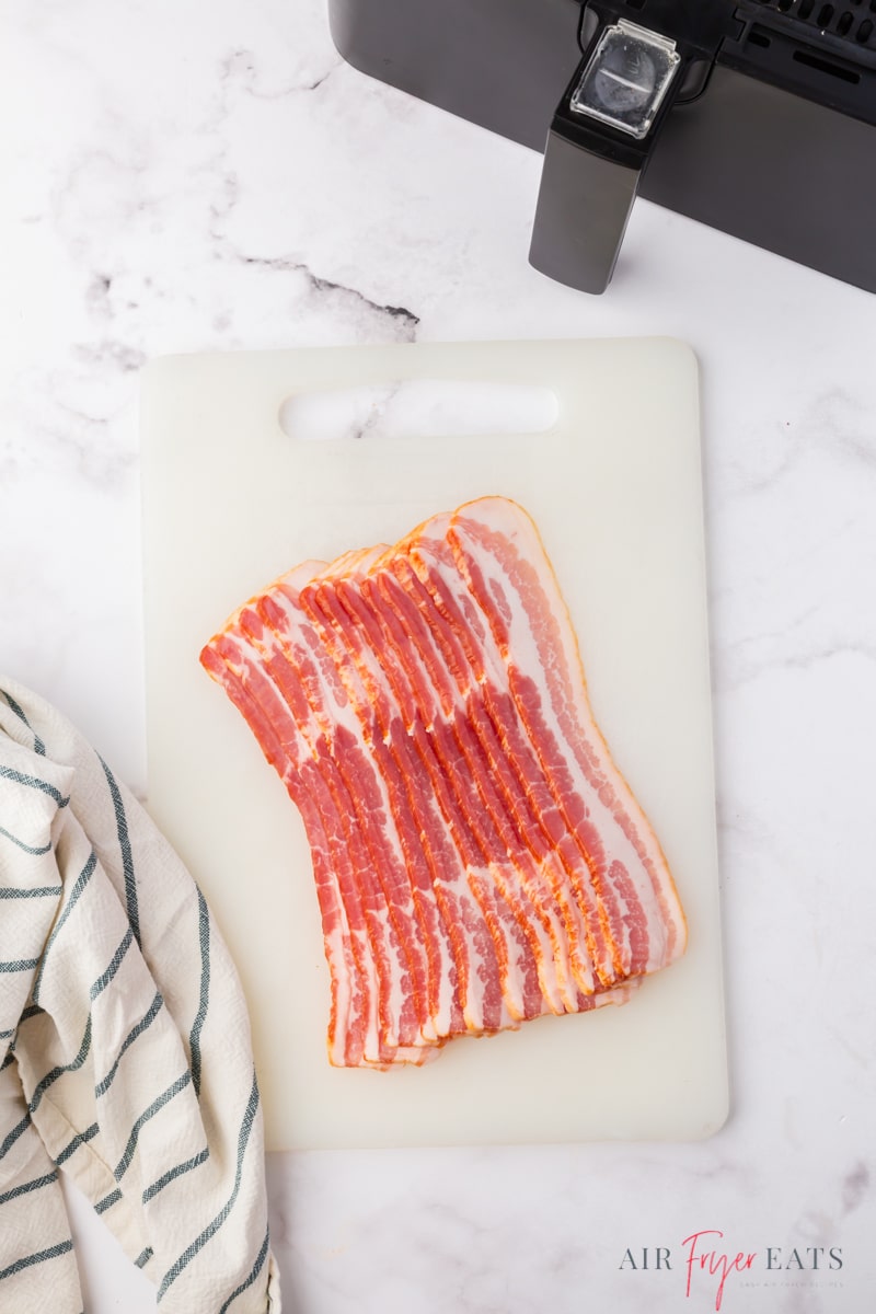 a slab of raw sliced bacon on a plastic cutting board in front of a cosori air fryer