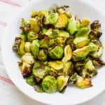 roasted brussels sprouts in a white bowl over a red and white striped towel