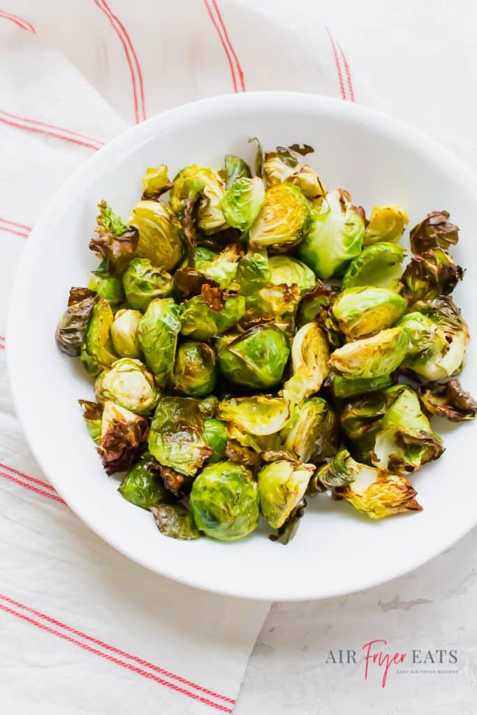 roasted brussels sprouts in a white bowl over a red and white striped towel