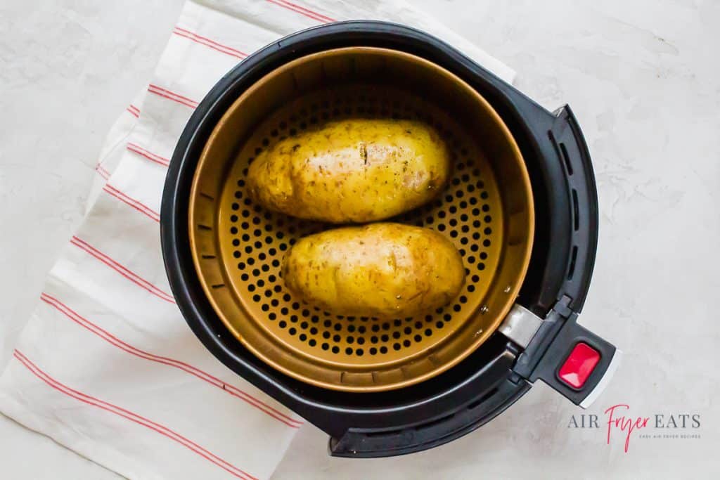 two brown russet potatoes in a round air fryer basket