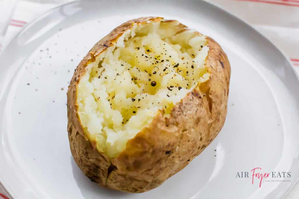 an air fryer baked potato split open with fresh cracked black pepper