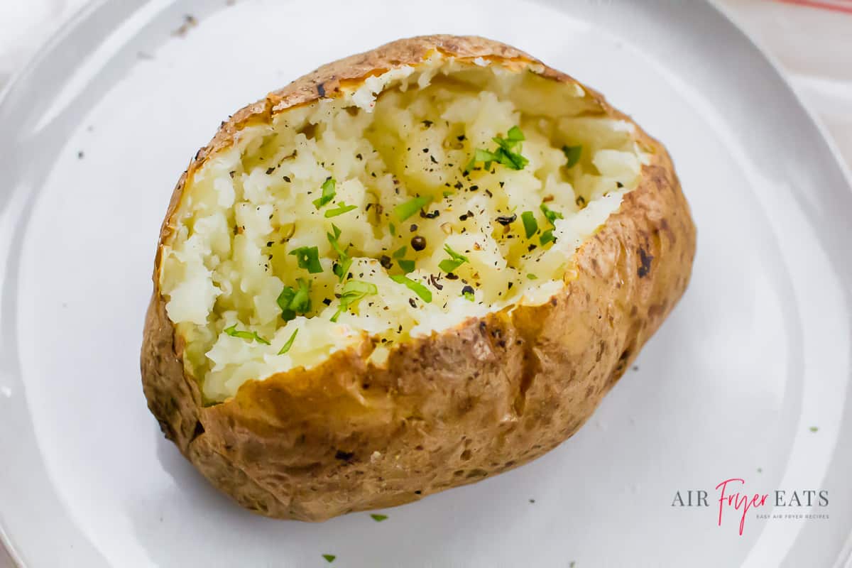 a baked potato split open and topped with green herbs