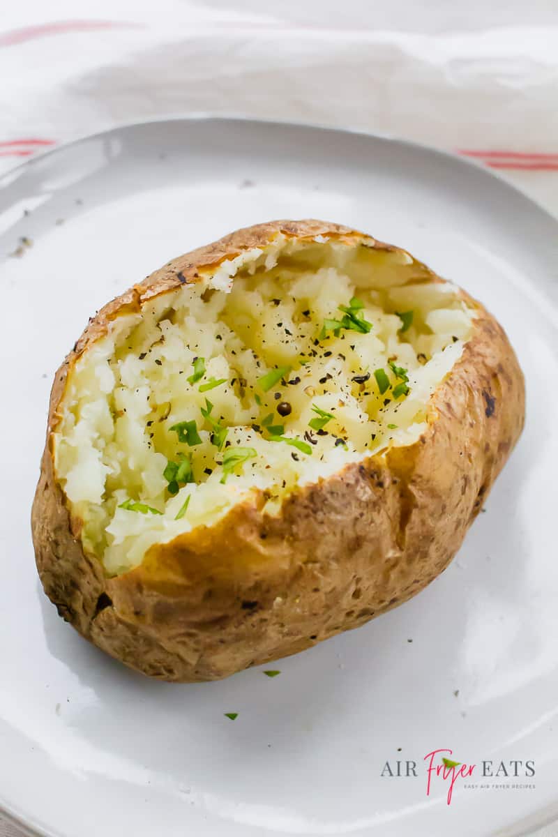 an air fryer baked potato split in half with herbs sprinkled overtop