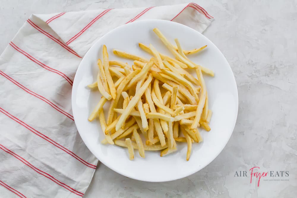 a pile of french fries on a round white plate over a red and white striped towel