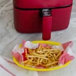 a yellow basket of cooked french fries beside a red air fryer