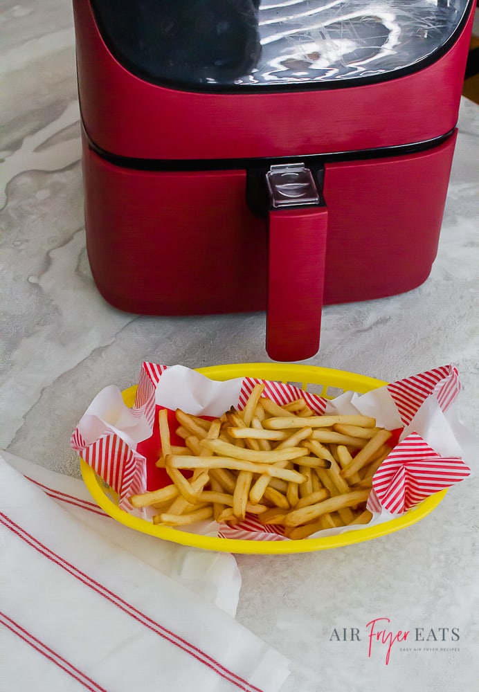 a yellow basket of cooked french fries beside a red air fryer