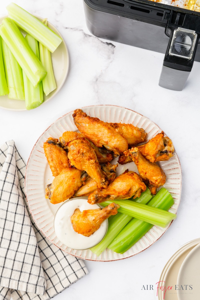 top down shot of a plate of chicken wings with a side of celery and a cup of ranch, sitting next to a cosori air fryer