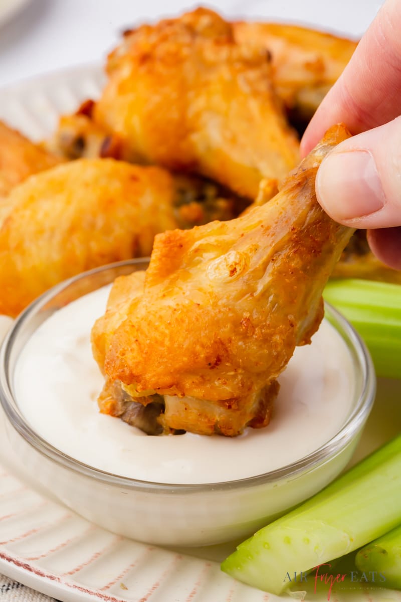 a hand dipping a chicken wing drumstick into ranch dressing.