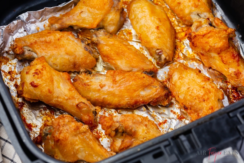 cooked chicken wings inside of an air fryer basket lined with aluminium foil