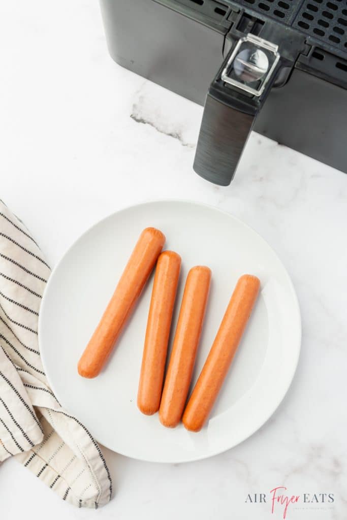 a white plate of four hot dogs next to a cosori air fryer, viewed from above