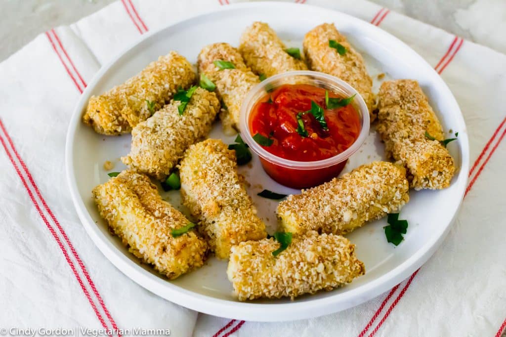 breaded mozzarella sticks with green herbs on top with red sauce in a plastic container in the middle of a white dish