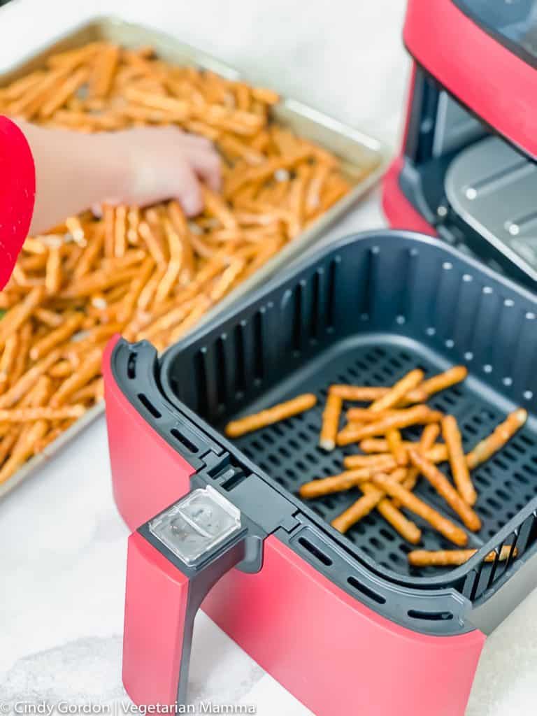 hand taking pretzels from baking sheet and transferring into a red air fryer basket.