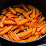 cooked orange carrot halves in an air fryer basket