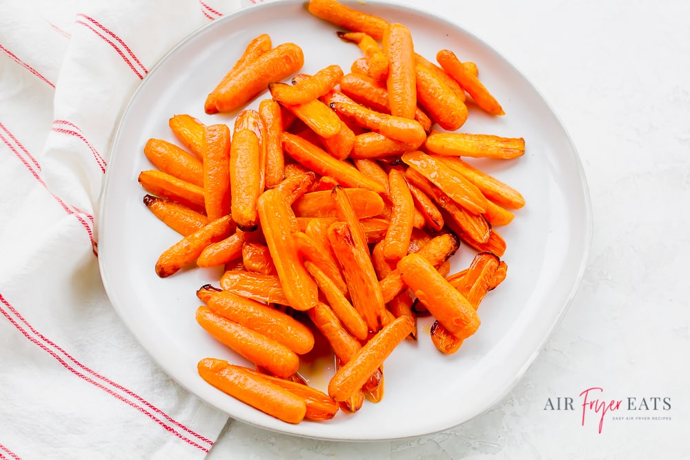 overhead shot of white plate containing orange carrot halves with white and red stripped napkin to the left. cooked  