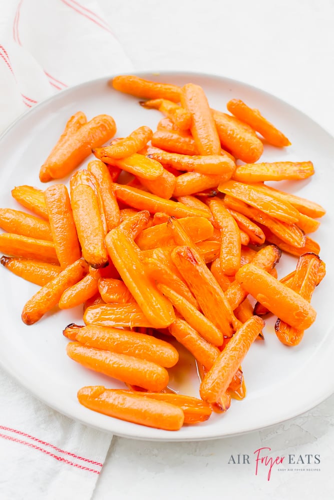 vertical photo of bright orange baby carrot halves on white plate - cooked  air fryer carrots