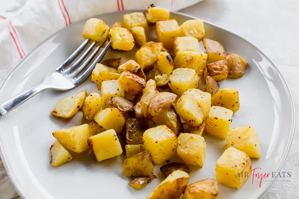 Close up shot of golden brown seasoned potato cubes on a white plate with a fork.