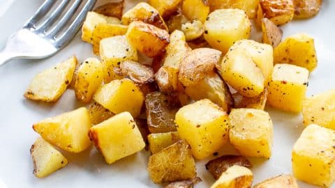 Crispy golden brown air fried potatoes on a white plate with a fork