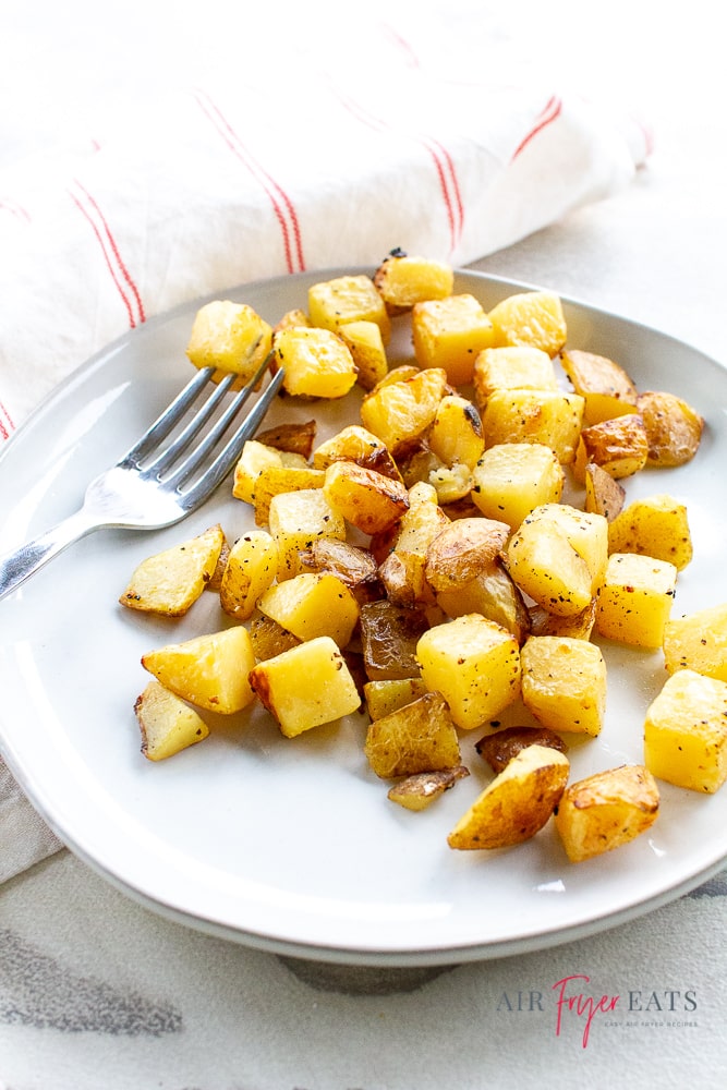 vertical shot of golden brown seasoned potatoes on plate with white napkin with thin red stripes and a fork pictured